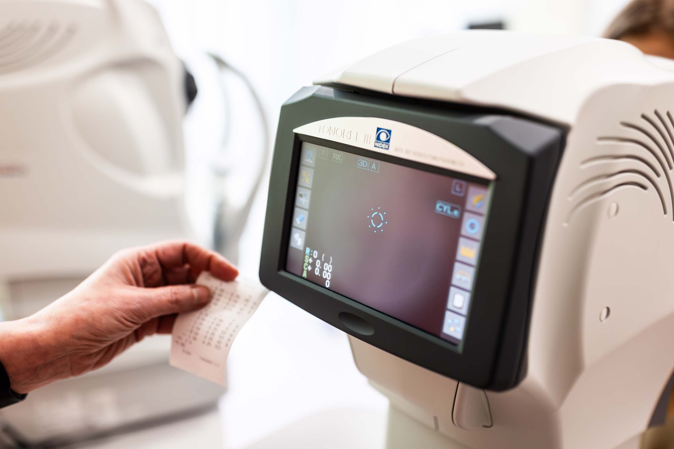 Presná diagnostika zraku pomocou moderného autorefraktometra Detail autorefraktometra počas merania zraku, lekár drží vytlačený výsledok vyšetrenia.