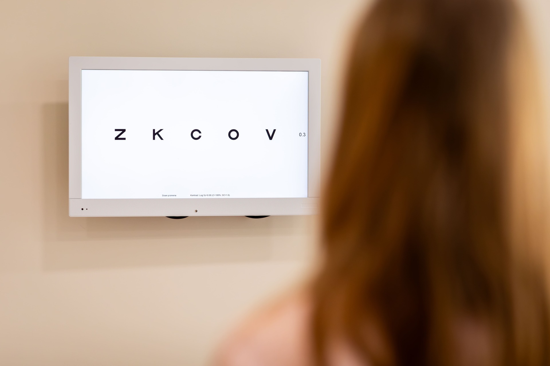 Pacientka číta písmená z LCD optotypu počas vyšetrenia zraku u očného lekára.